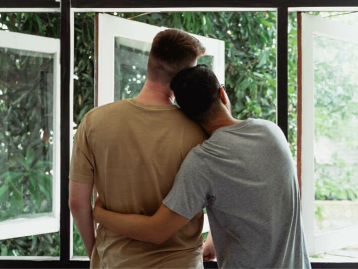 Two men hugging in front of a window.