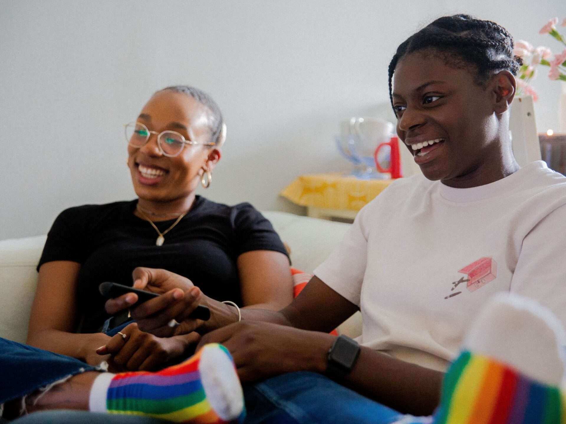 Two women sitting on a couch with rainbow socks.