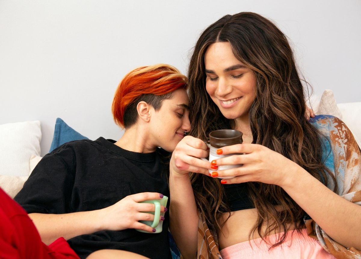 Two women sitting on a couch with a cup of coffee.