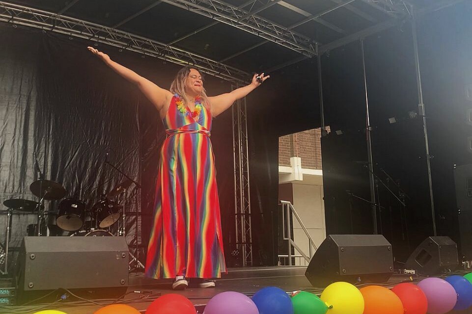 A woman in a rainbow dress on stage with balloons.