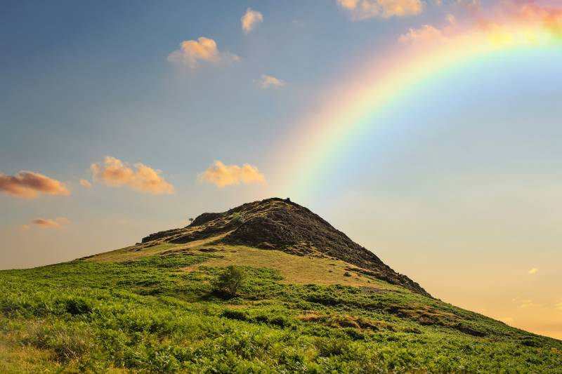 A rainbow is seen over a green hill.