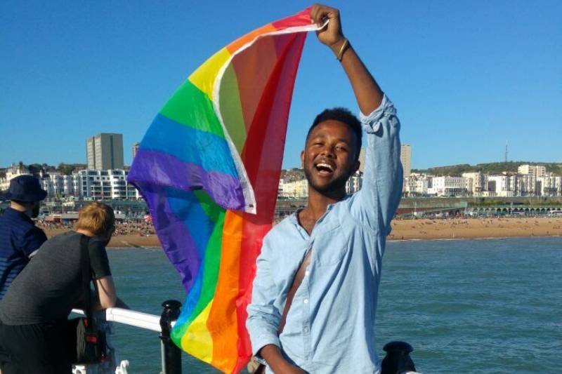 A man holding a rainbow flag on a pier.