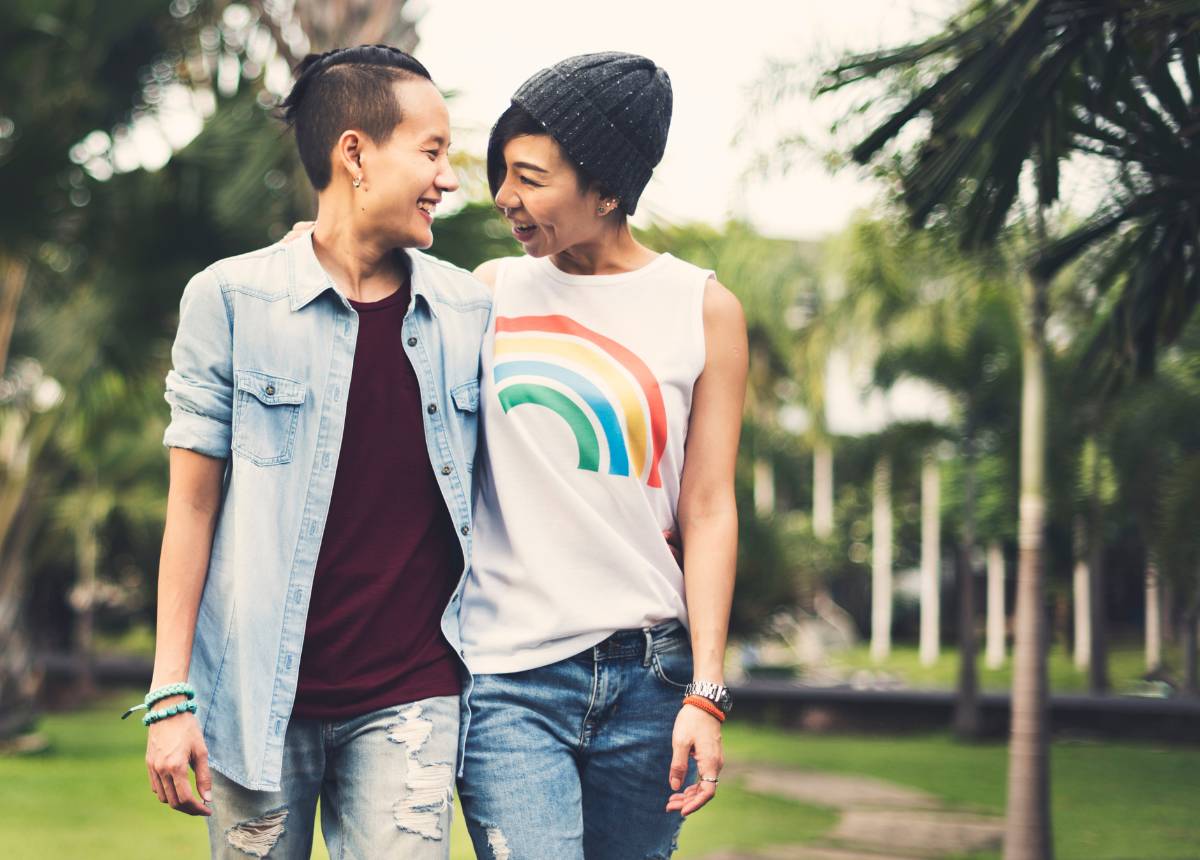 Two asian people standing in a park with rainbow t - shirts.