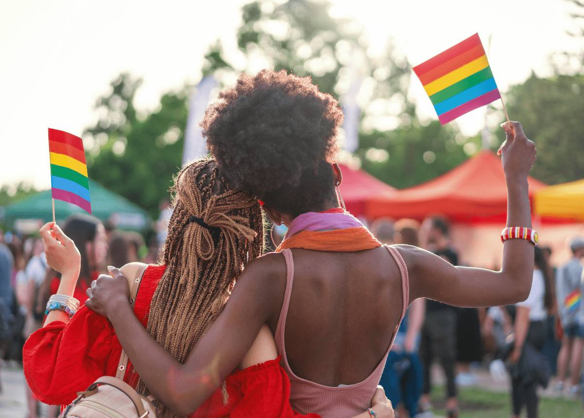 Two women holding rainbow flags at an outdoor LGBT event in Rwanda.