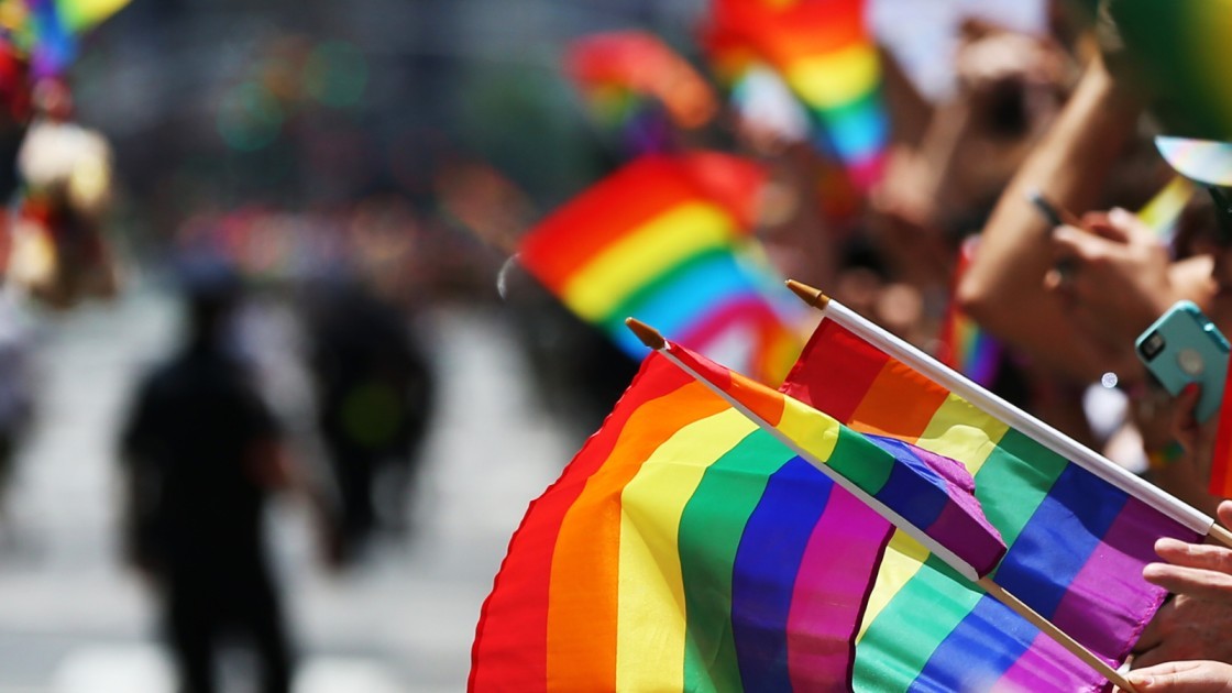 A group of people waving rainbow flags in a parade that showcases LGBTQI+ solidarity and pride.
