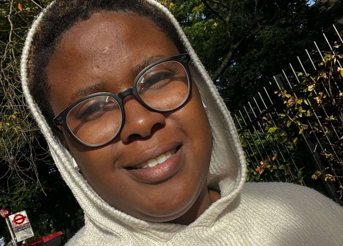 A woman wearing glasses and a hoodie smiles for the camera during a campaign.