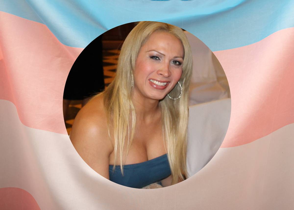 A transgender woman posing in front of a flag.