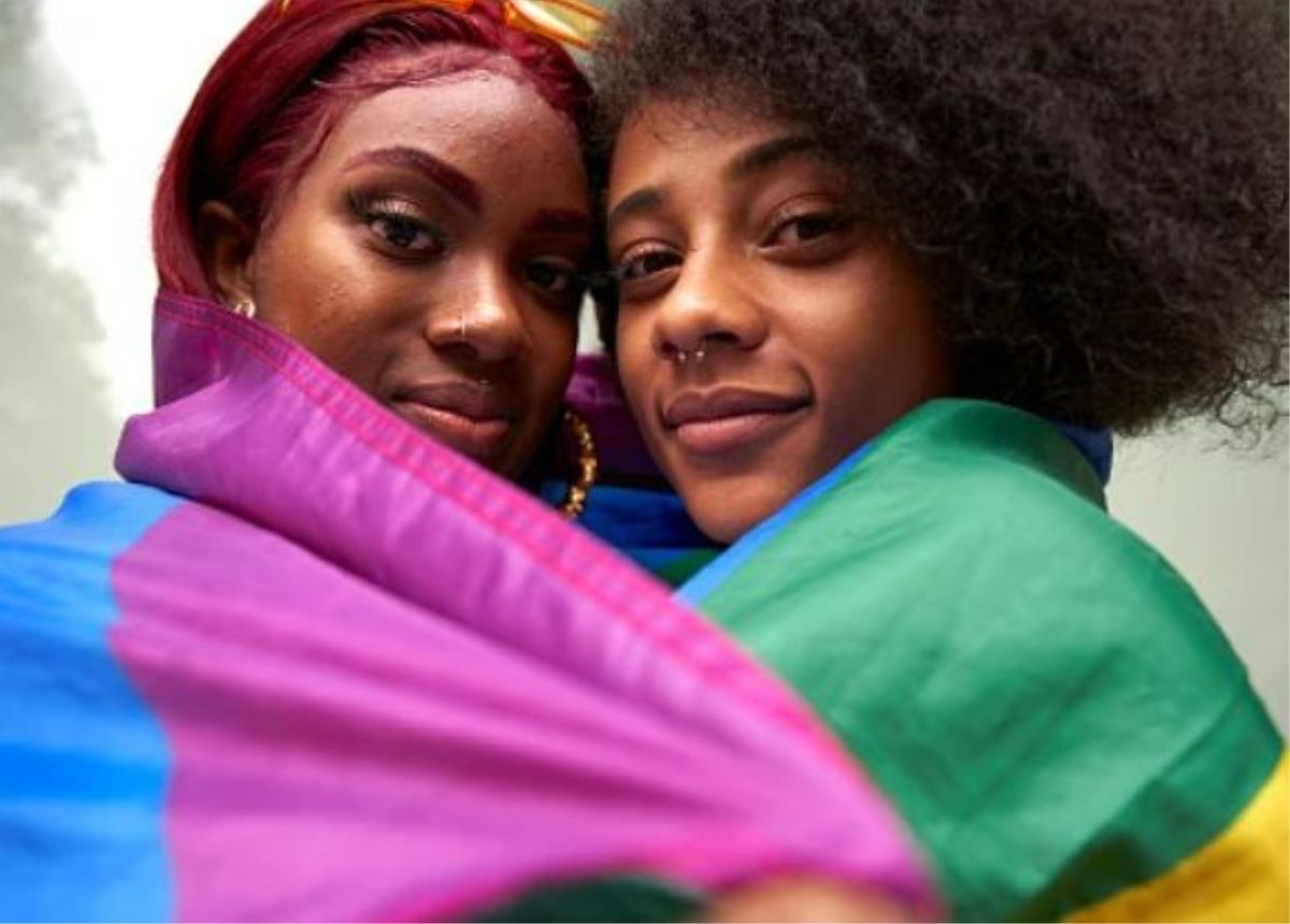 Two black women posing for a photo with a rainbow flag.