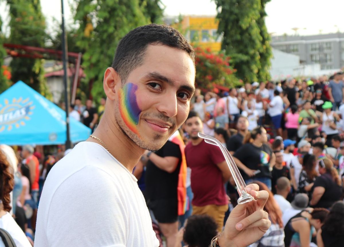 A man with a rainbow colored face is holding a straw.