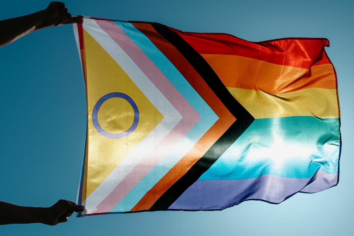 A person holding a rainbow flag in front of a blue sky.