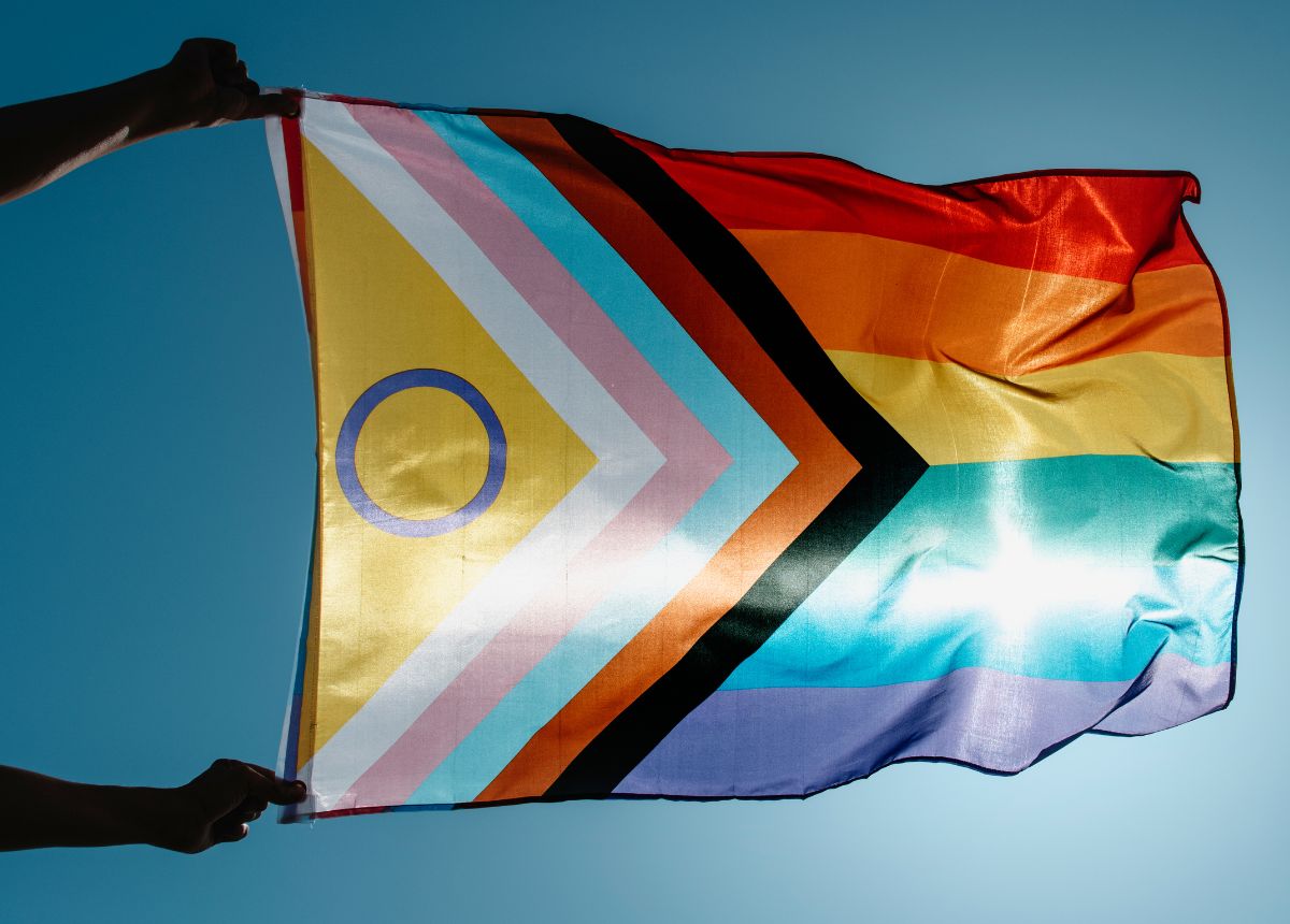 A person holding a rainbow flag in front of a blue sky.