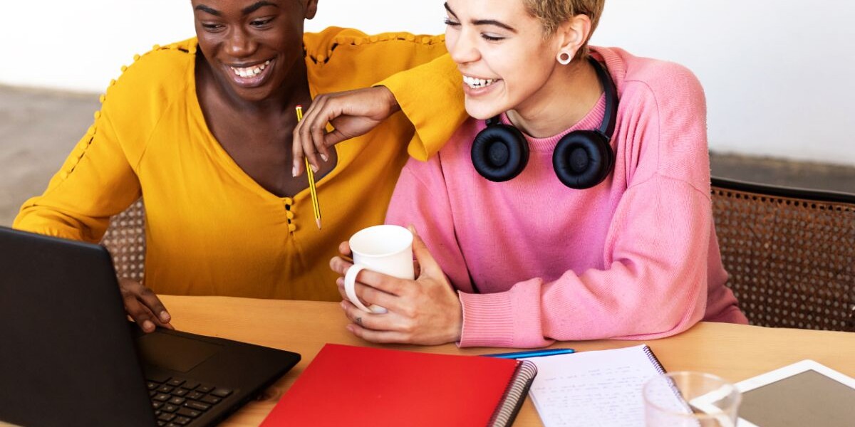 two queer women in front of laptop laughing